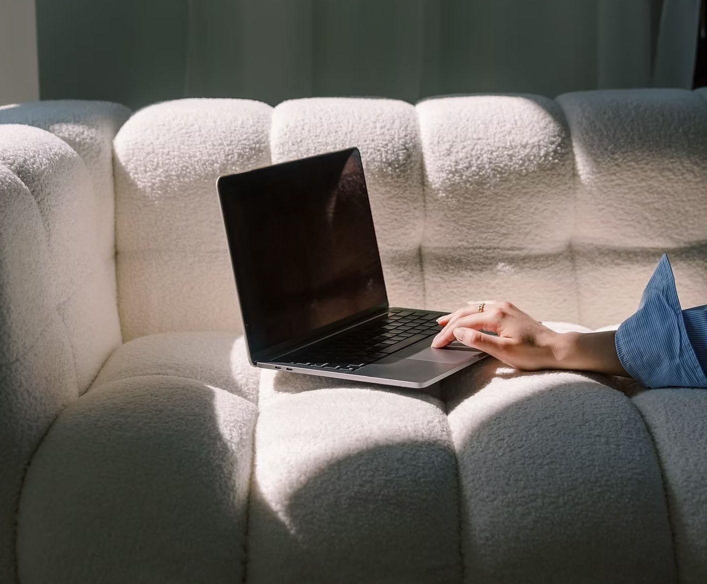 Mains posées sur un canapé blanc tapant sur le clavier d’un MacBook, vue de profil