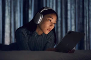Jeune fille allongée sur son lit, casque sur les oreilles, concentrée en regardant sa tablette