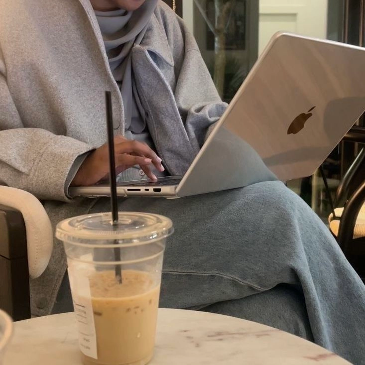 Ordinateur portable posé sur les jambes d’une femme, avec un verre de mocca à côté, elle tape sur le clavier